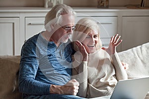 Excited aged couple winning lottery online at laptop