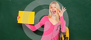 Excited amazed teacher. Student girl holding empty faper for product. Portrait of smiling female teacher near blackboard