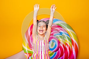 excited arab child girl in colorful striped dress raising her arms in the air having fun on yellow background