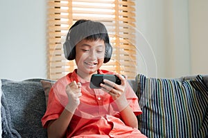 Excited Asian boy playing online game on smart phone with headphones. Asia man using mobile phone happy smile at home in morning