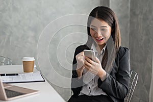 Excited asian business girl while reading a smart phone sitting