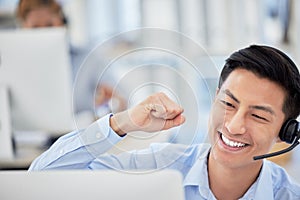 Excited asian businessman celebrating a success cheering and punching the air with his fists as he sits at a desk. One