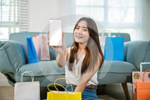 Excited Asian buying woman smiling showing mobile phone with many shopping bags