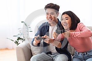 Excited Asian Couple Playing Videogames Sitting On Couch At Home