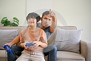 Excited Asian dad coaching his son to play video games with joysticks in the living room