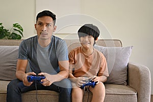 Excited Asian dad and son with joysticks are playing video games at home together