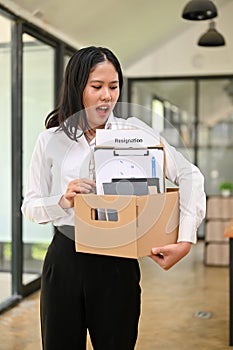 Excited Asian female office worker carrying her belonging, quitting a job