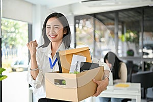 Excited Asian female office worker is celebrating her resignation, carrying her personal stuff