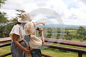 Excited asian kid looking through binocular searching for animal with her mother in savannah green forest.