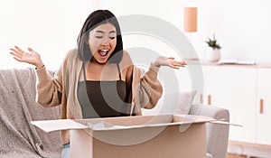 Excited asian woman unpacking parcel after online shopping photo