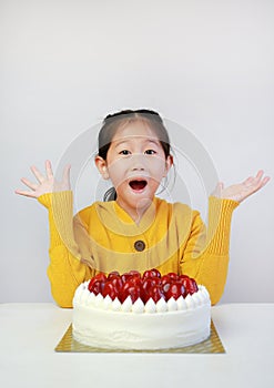 Excited asian little girl with strawberry cake. Kid with happy birthday cake on the table