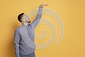 Excited Asian Man Measuring High Invisible Object With Hand Over Yellow Background