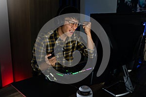 Excited asian man pro gamer sitting at the table, playing and Winning in online video games on a computer and smartphone,