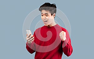 Excited asian man using mobile phone, celebrating online win