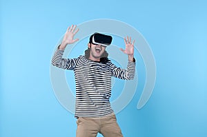 Excited Asian man wearing virtual reality goggles watching movies on blue background