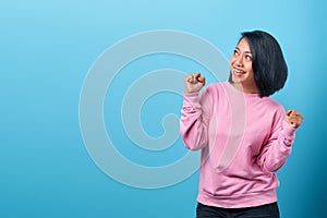 Excited asian woman celebrating success with two fists in the air and looking up empty space