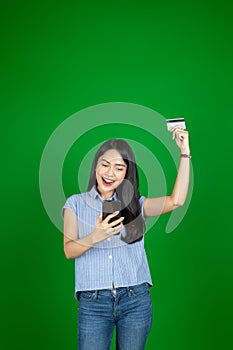 excited asian woman using a mobile phone while holding atm card with raised hand