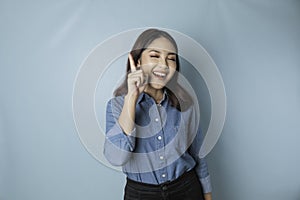 Excited Asian woman wearing blue shirt pointing at the copy space upwards,  by blue background