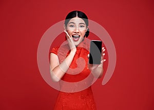 Excited Asian woman wearing traditional cheongsam qipao dress showing mobile phone isolated on red background