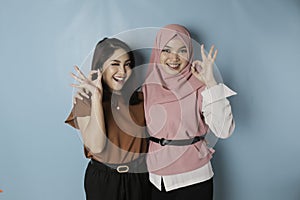 Excited Asian women giving an OK hand gesture isolated by a blue background