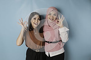 Excited Asian women giving an OK hand gesture isolated by a blue background