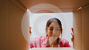 Excited Asian young woman unpack opening huge carton box and looking inside new gift at home.