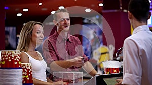 Excited attractive young happy guy girl couple making popcorn order from male cashier worker at cinema movie theater