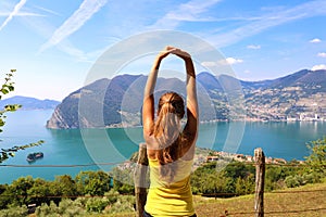 Excited attractive young woman in sportswear stretching enjoying Lake Iseo landscape in the morning, North Italy. Cheerful mood