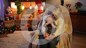 Excited baby girl clapping in slow motion sitting with young woman in rocking chair indoors. Portrait of happy cheerful