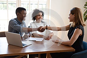 Excited biracial couple handshake agent closing deal at meeting