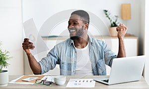 Excited black businessman checking financial reports and celebrating success