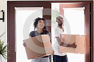 Excited black couple carrying boxes impressed entering new home