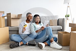 Excited black couple choosing furniture online, buying goods for their new flat, using digital tablet and credit card