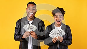 Excited Black Couple Holding Money Cash Standing Over Yellow Background