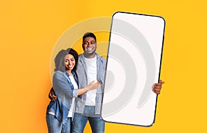 Excited black couple showing white empty smartphone screen