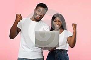 Excited black couple using laptop celebrating success shaking fists