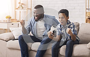 Excited Black Father And Son Watching Sports On TV And Cheering