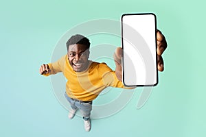 Excited black guy demonstrating smartphone with blank white screen, showing free copy space for your ad, mockup