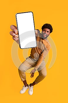 Excited black guy holding smartphone, jumping up photo