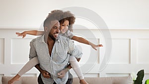 Excited black man giving piggyback ride to happy cute daughter.