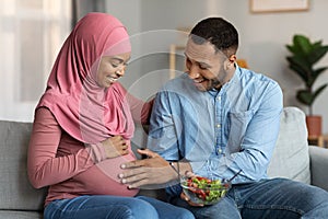 Excited Black Man Tenderly Touching Pregnant Muslim Wife& x27;s Belly, Feeling Baby Kicks