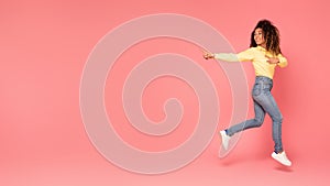 Excited black woman jumps, pointing aside at copy space on pink backdrop, panorama