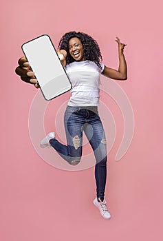 Excited black woman showing smarthone with blank white screen to camera, jumping with modern gadget, mockup