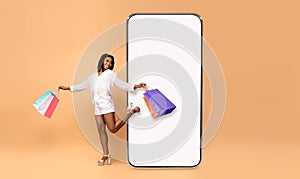 Excited black woman walking out cell screen with shopping bags