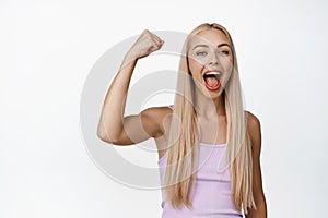 Excited blond girl rooting for someone, chanting and screaming happy, making fist pump for encouragement, standing