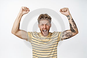 Excited blond guy rooting, winning prize and raising hands up to celebrate, achieve goal and celebrating victory
