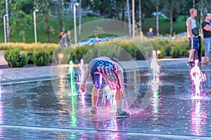 Excited boy plays on city illuminated fountain water springs