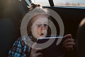 Excited boy watching a movie on technology tablet in car. Child using computer.