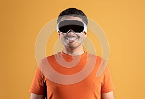 Excited brazilian man wearing vr vision pro glasses, using virtual reality for entertainment on orange studio background