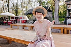 Excited brunette girl in trendy hat received message from friend and laughing. Portrait of joyful young woman in vintage